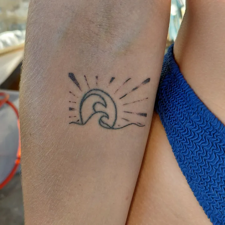 Cover-up, after: a wave with sun rays added around it, on the forearm