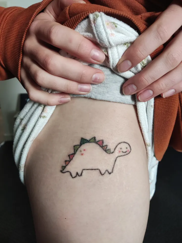 Cover-up, after: the dinosaur redrawn with clean lines and colour, on the thigh