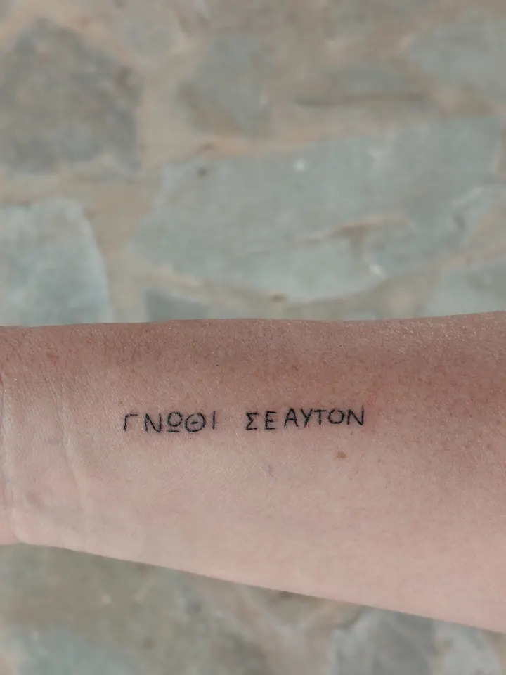 ΓΝΩΘΙ ΣΕΑΥΤΟΝ (know thyself) in Greek capitals on the forearm