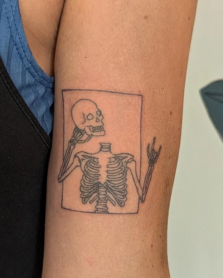 Skeleton in a frame making the rock hand sign, on the upper arm